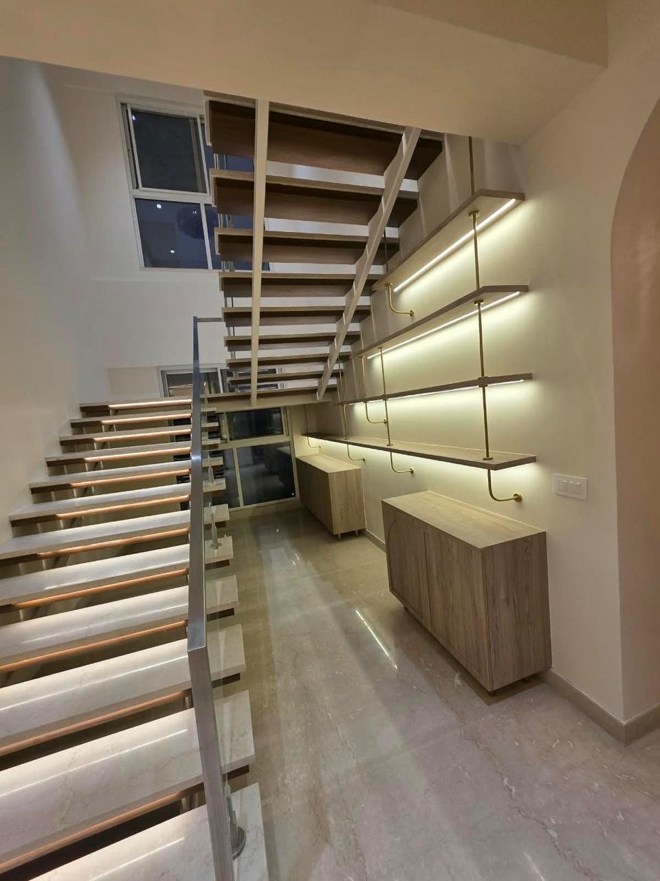 Floating staircase with lit treads and brass-supported wall shelving